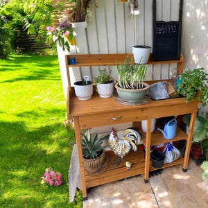 May include: A wooden garden potting bench with a shelf and a drawer. The bench has several potted plants, a watering can, and a decorative rooster figurine.
