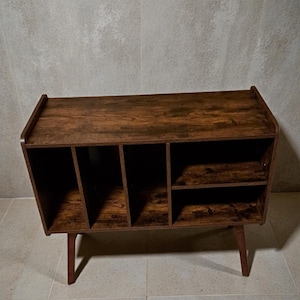 May include: A brown wooden storage cabinet with multiple compartments and shelves. The cabinet has a mid-century modern design with angled legs and a wood grain finish. It is suitable for storing various items.