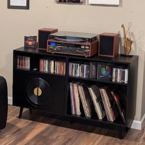 Puede incluir: Mueble de entretenimiento negro con tocadiscos, altavoces y almacenamiento para discos de vinilo y CD. El tocadiscos es marr&oacute;n y plateado. Una escultura de saxof&oacute;n dorado se encuentra encima del mueble.