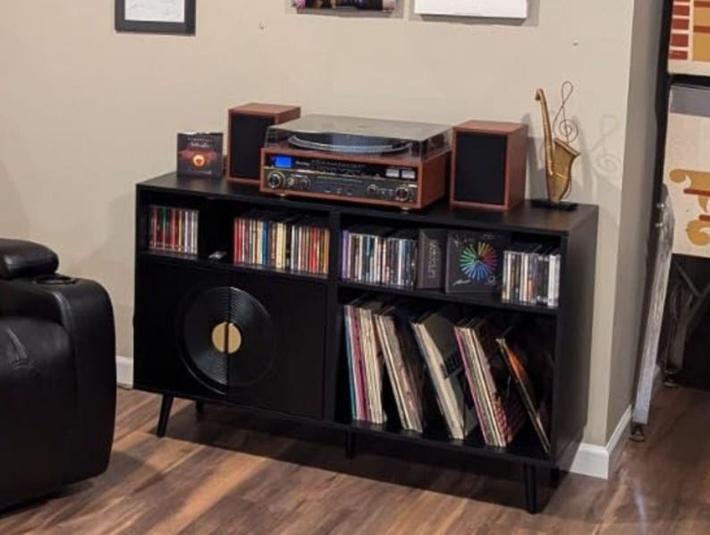 Puede incluir: Mueble de entretenimiento negro con tocadiscos, altavoces y almacenamiento para discos de vinilo y CD. El tocadiscos es marr&oacute;n y plateado. Una escultura de saxof&oacute;n dorado se encuentra encima del mueble.