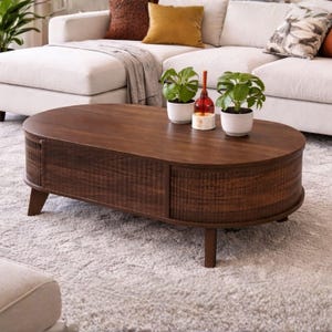 May include: A dark brown, oval-shaped coffee table with a textured, slatted design on the sides. The table has four short, angled legs and is topped with two potted plants and a decorative bottle. The table is placed on a light gray rug.