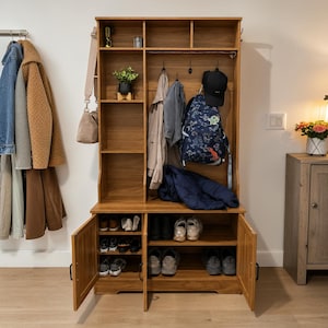 May include: A tall wooden hall tree with a light brown finish, featuring open upper shelving, a central coat rack with hooks, and a lower storage cabinet with two doors. The unit holds various items including a backpack, jackets, and shoes.
