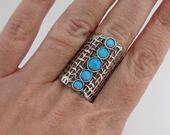 Puede incluir: Un anillo de plata con un diseño geométrico y ópalos azules. El anillo es ancho y tiene una superficie texturizada.