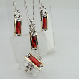 May include: A silver and gold necklace, earrings, and ring set with red gemstone accents. The jewelry features a delicate, ornate design.