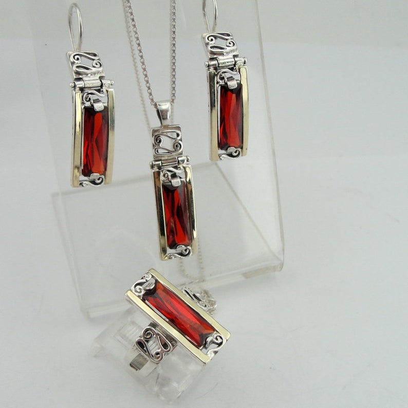 May include: A silver and gold necklace, earrings, and ring set with red gemstone accents. The jewelry features a delicate, ornate design.