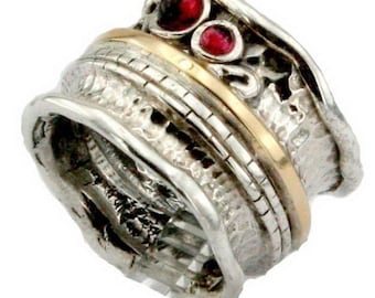 Może przedstawiać: Srebrny i złoty pierścionek z fakturowanym wykończeniem i dwoma czerwonymi kamieniami szlachetnymi. Pierścionek jest zaprojektowany do obracania.