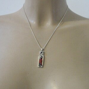 May include: A silver chain necklace with a pendant featuring a rectangular red gemstone surrounded by silver filigree.