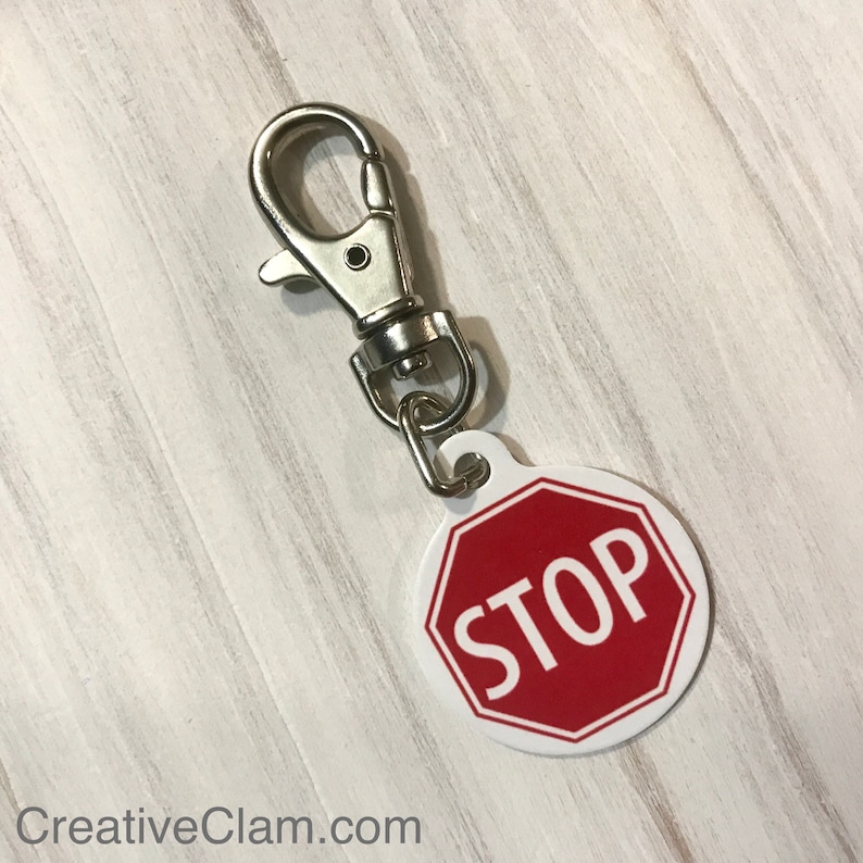 May include: A silver key chain with a round red stop sign with white lettering that says "STOP".