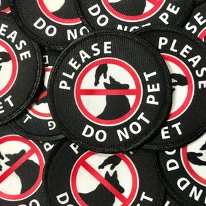 May include: A set of round black and white patches with red circles and the text "Please Do Not Pet" in white. The patches feature a silhouette of a dog's head with a hand reaching out to pet it, crossed out with a red circle.