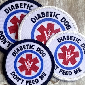 May include: Three white round patches with blue and red accents. Each patch has a red star of life symbol with a snake wrapped around a rod in the center. The text on the patches reads "Diabetic Dog Don't Feed Me".