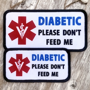 May include: Two white rectangular patches with black borders. The patches have a red medical symbol with a snake and a staff, and the text "DIABETIC PLEASE DON'T FEED ME" in black and blue.