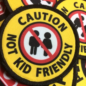May include: Yellow round patch with black stitching around the edge. The patch has a red circle with a diagonal red line through it. Inside the red circle are two black stick figures. The text on the patch reads "CAUTION NOT KID FRIENDLY".