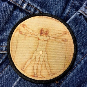 May include: A round, beige patch with a black border, featuring a line drawing of a nude figure in a circle, with arms outstretched, reminiscent of Leonardo da Vinci's Vitruvian Man.