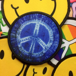 May include: A blue peace sign patch with a white tie-dye pattern. The patch is surrounded by other patches, including smiley faces and rainbow designs.