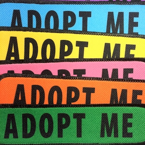 May include: Five colorful fabric patches with the text "Adopt Me" in black lettering. The patches are in the colors purple, blue, yellow, pink, and orange.