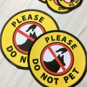 May include: Two yellow and black round patches with the text "Please Do Not Pet" and a red circle with a diagonal line through it. The circle contains a black silhouette of a dog and a hand reaching down to pet it.