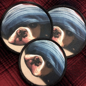 May include: Three round fabric patches with a close-up image of a brown and white dog's nose and mouth. The dog is wearing a blue and white striped bandana over its eyes.
