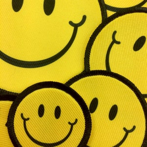 May include: A close-up of four yellow smiley face patches with black outlines. The patches are arranged in a random pattern, with some overlapping.