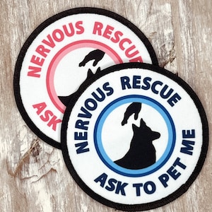 May include: Two white round patches with black borders. The top patch has a pink circle with the text "NERVOUS RESCUE ASK" and a silhouette of a hand reaching out. The bottom patch has a blue circle with the text "NERVOUS RESCUE ASK TO PET ME" and a silhouette of a hand reaching out to a dog.