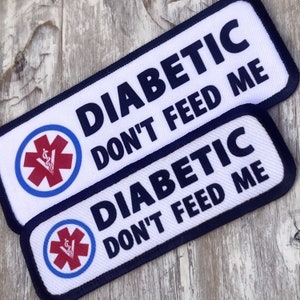 May include: Two white patches with blue borders and a red medical symbol. The text "DIABETIC DON'T FEED ME" is printed in black on each patch.