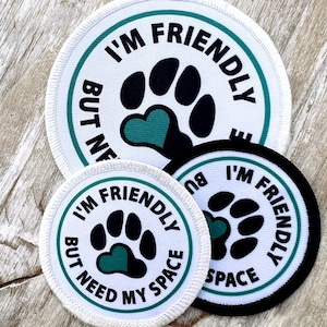 May include: Three white and black round patches with green text and a paw print with a green heart. The text on the patches reads "I'm Friendly But Need My Space".