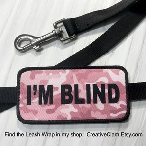 May include: Pink camouflage leash wrap with black text that reads "I'M BLIND".