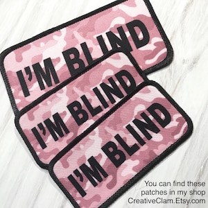 May include: Three pink camouflage fabric patches with black text that reads "I'M BLIND".