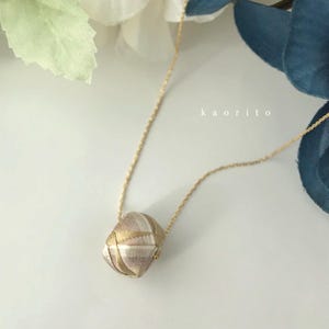 May include: A gold-tone chain necklace featuring a geometric, multi-faceted pendant wrapped in metallic gold and silver thread. The pendant displays a complex, woven pattern of intersecting lines. The text kaorito is visible in the background.