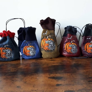 Peut inclure: Cinq petits sacs à cordon avec un motif de chat et de citrouille. Les sacs sont de différentes couleurs : rouge, bleu, vert, bordeaux et noir.