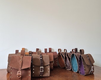 Könnte beinhalten: Eine Sammlung brauner Ledertaschen mit Schnallen und Metallverzierungen. Die Taschen sind in einer Reihe auf einer Holzoberfläche angeordnet.
