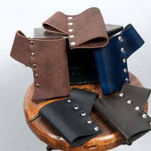 May include: Five leather wrist cuffs with silver metal rivets. The cuffs are in various colors, including brown, dark brown, black, and blue.