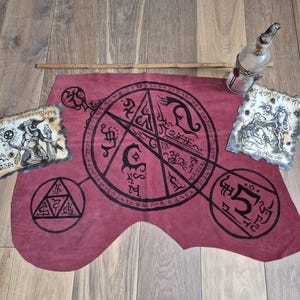 May include: A red leather cloth with a black pentagram design and other symbols. The cloth is surrounded by three pieces of paper with black ink drawings.