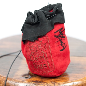 May include: Red suede dice bag with a black drawstring and the words "Devil Dust" embroidered on the front.