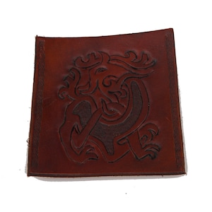 May include: A brown leather coaster with a Celtic knot design featuring a stylized animal, possibly a dragon or a wolf.