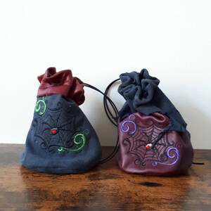 May include: Two small, drawstring bags with embroidered spiderwebs and red beads. One bag is dark blue with green embroidery and the other is burgundy with purple embroidery.