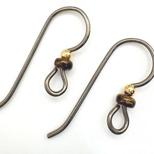 May include: A pair of handcrafted earrings featuring dark gray metal hooks with a small loop at the bottom. Each earring has a dark brown bead and a small gold-colored bead. The earrings are displayed against a white background.