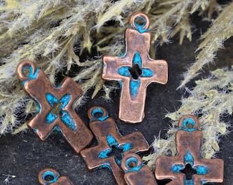 May include: A collection of five copper-toned metal cross charms, each featuring a central star-shaped cutout and a weathered finish with bright turquoise patina accents in the recessed areas. Each cross includes a small circular loop at the top.