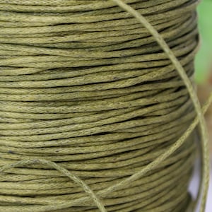 May include: A close-up of a spool of green waxed cotton cord. The cord is tightly wound and has a slightly textured surface.
