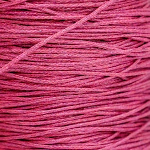 May include: Close-up of a spool of vibrant magenta-colored twine. The tightly wound cord is made of numerous thin strands, creating a textured surface. This craft supply is suitable for various DIY projects.