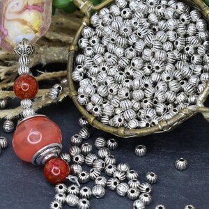 May include: A bowl filled with silver metal beads with a ribbed texture. The beads are scattered on a dark gray surface.
