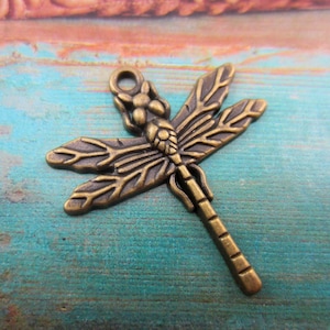 May include: Bronze-colored dragonfly charm with detailed wings and body. The charm has a loop at the top for attaching to jewelry or other crafts. The dragonfly is a popular symbol in jewelry and craft making.