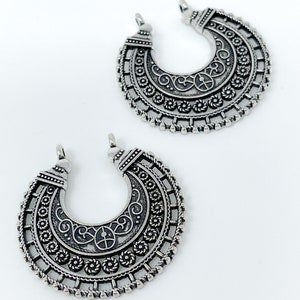 May include: Two silver crescent moon shaped pendant charms with intricate filigree designs.