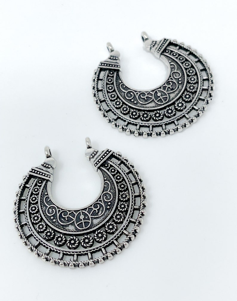 May include: Two silver crescent moon shaped pendant charms with intricate filigree designs.