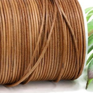May include: A spool of brown leather cord. The cord is tightly wound, revealing a textured surface and a warm, natural color. The image is well-lit, highlighting the details of the leather. The cord is suitable for jewelry making and crafts.