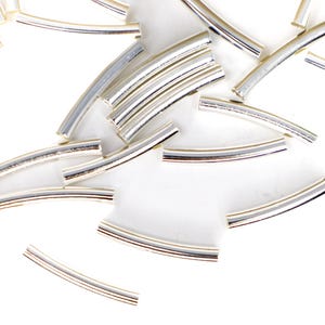 May include: A collection of silver-colored, curved metal tubes scattered on a white surface. Each tube has multiple parallel lines in shades of silver and gray, creating a striped effect. The tubes are slightly rounded, suggesting they could be used as jewelry components.