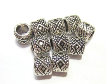 May include: A collection of small, cylindrical silver-toned metal beads featuring a textured surface with a raised diamond pattern and dotted detailing. Each bead has a central hole, and the metal has an oxidized finish in the recessed areas.