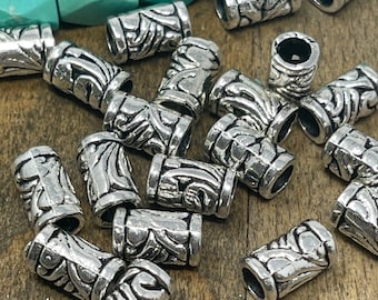 May include: A pile of silver metal beads with an intricate design. The beads are cylindrical and have a textured surface.