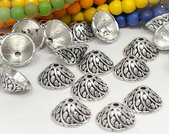 Op de afbeelding: Een verzameling zilverkleurige metalen kralenkapjes met een decoratief swirl-patroon. De kapjes zijn kegelvormig en hebben een klein gaatje bovenaan om in te rijgen.