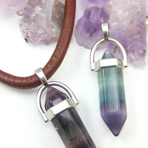 May include: Two silver and crystal point pendants on a brown leather cord. The pendants are shaped like a point and have a silver ring around the top. The crystals are purple and green.