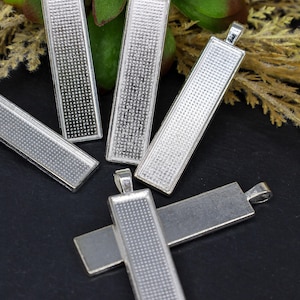 May include: Five silver-toned metal pendant trays with a textured surface. The trays are rectangular and have a loop at the top for hanging.